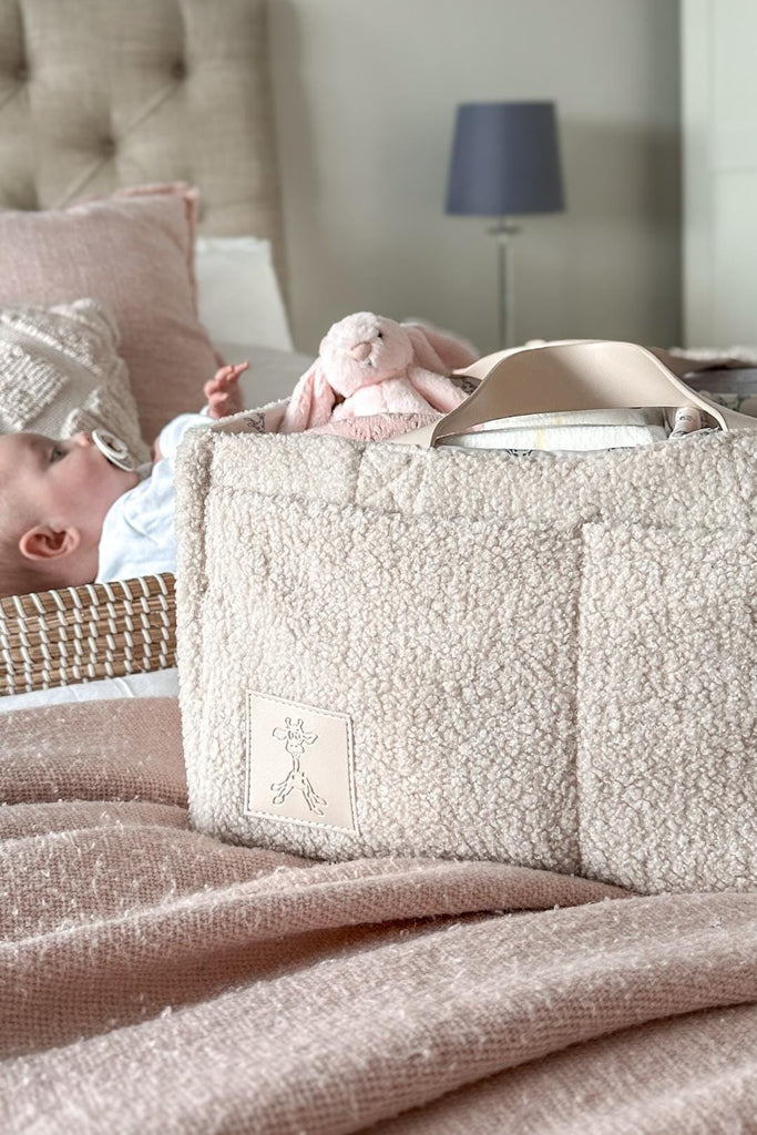 Beige teddy nappy caddy next to a baby on a bed with the gigil giraffe logo 