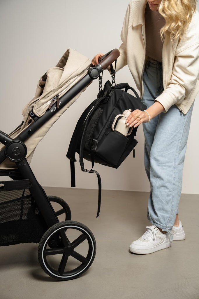 Coast Bag hanging from buggy whilst mother places her child's bottle into the side pocket of the bag.