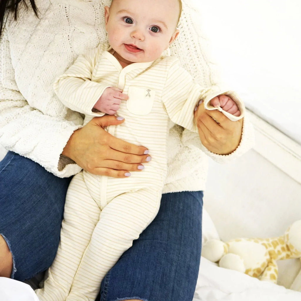 A baby sitting in a woman's lap wearing a thin neutral stripe organic baby sleepsuit