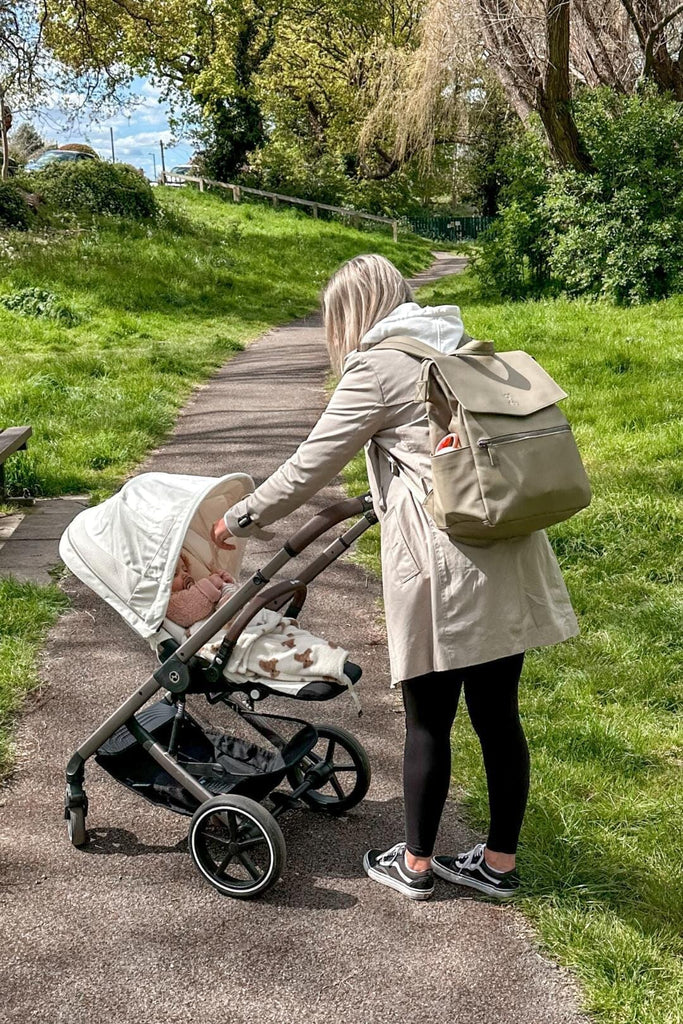 Mum in a park pushing a pram wearing olive green vegan leather baby changing backpack 