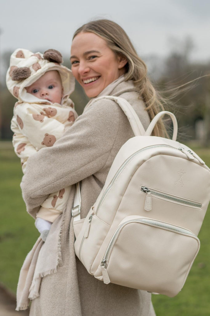 Mum holding a baby and wearing the sand beige bloom diaper backpack 