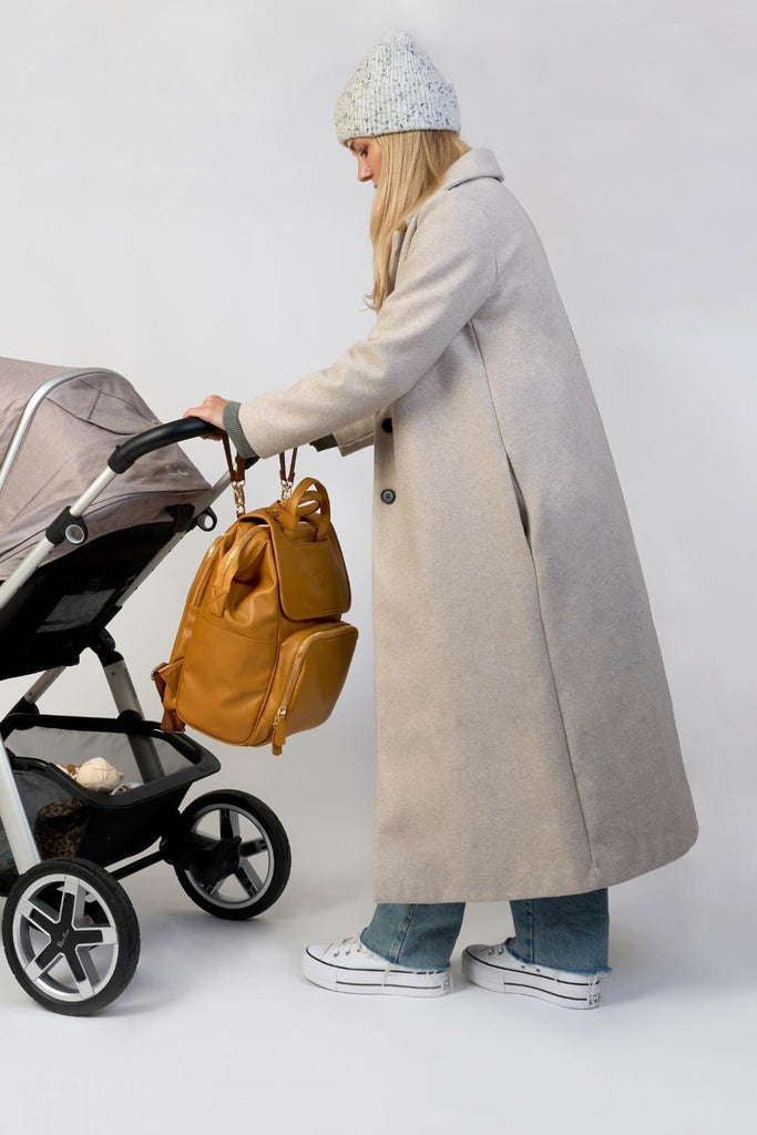Tan vegan leather changing backpack hanging from pram with matching pram clips