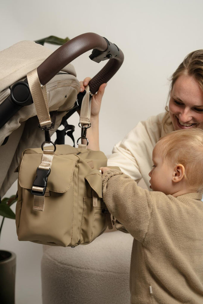 Nala Buggy Organiser hanging from a pram whilst mother and child clip the buckle fastener closed.