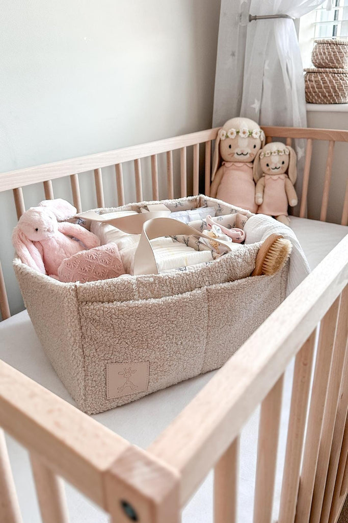Cream teddy nappy caddy filled with baby essentials in a cot in a nursery