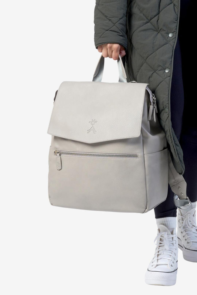 Mum carrying a grey vegan leather backpack by the top handle with zipped front pocket and gigil giraffe logo 