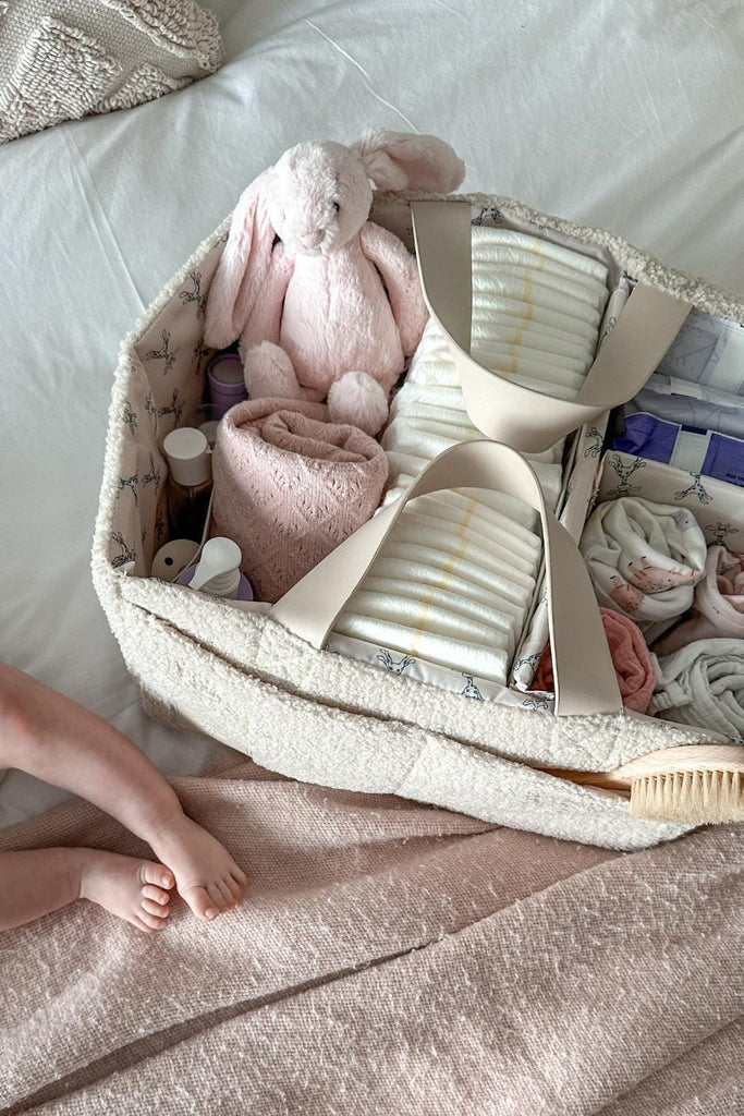 Top down view of cream teddy nappy caddy filled with nappies and baby essentials 