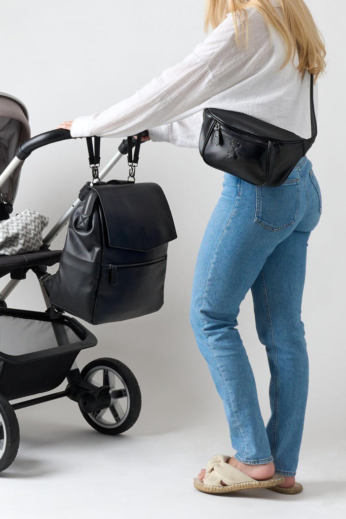 Vegan leather backpack clipped to pram with matching pram clips and mum wearing vegan leather black buggy organiser