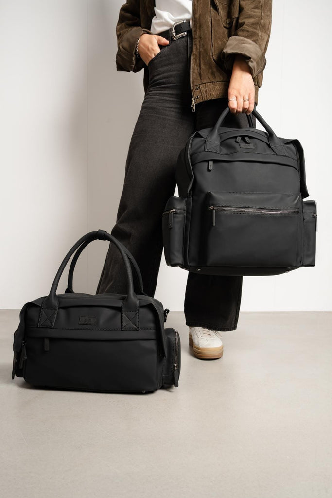 Willow Black Buggy Organiser sat on the floor whilst the model is holding the matching Coast Changing Bag with the carry handles.