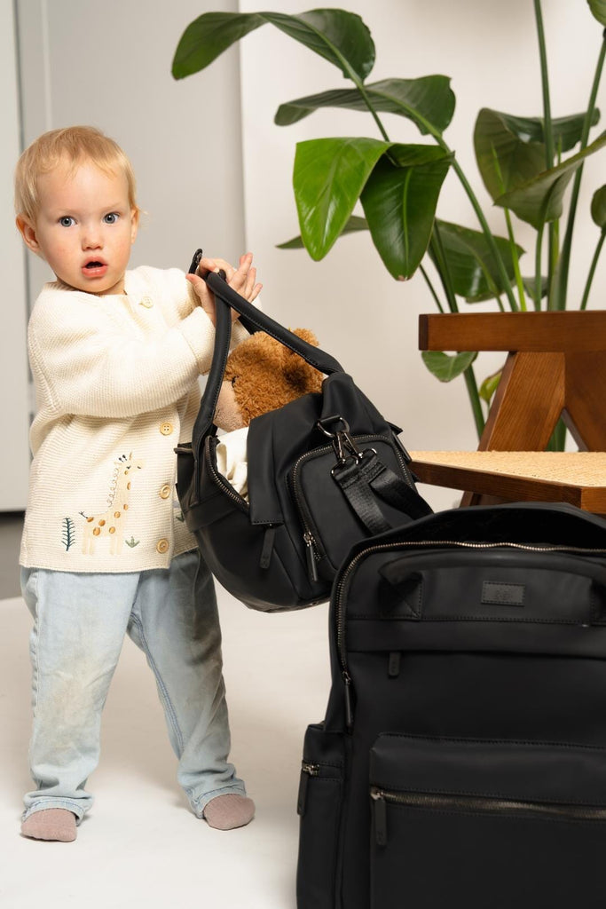 Coast Changing Backpack sat on the floor whilst a small child carries the matching Willow Buggy Organiser.