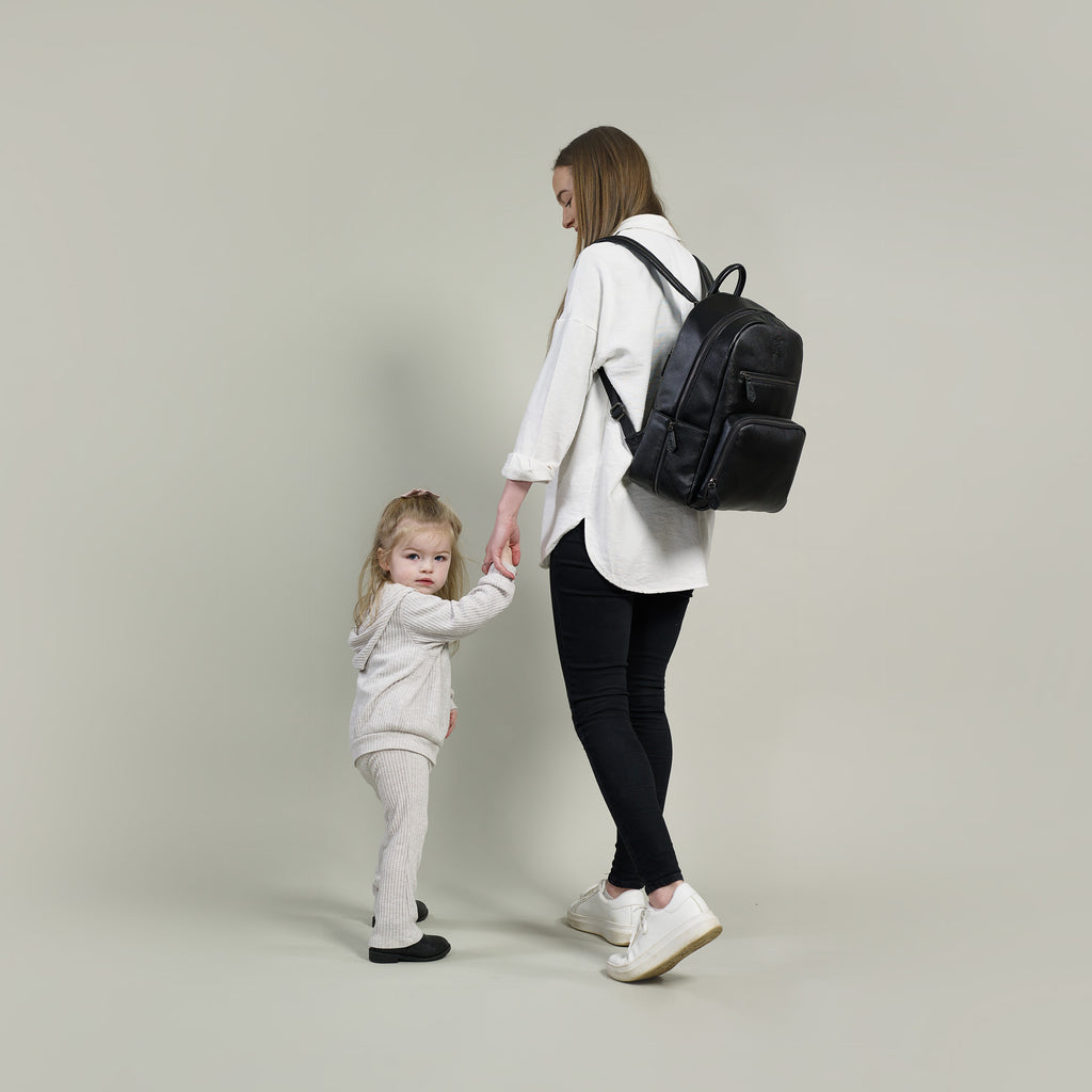Mum and toddler holding hands and a mum carrying the Gigil Bloom changing backpack in black 