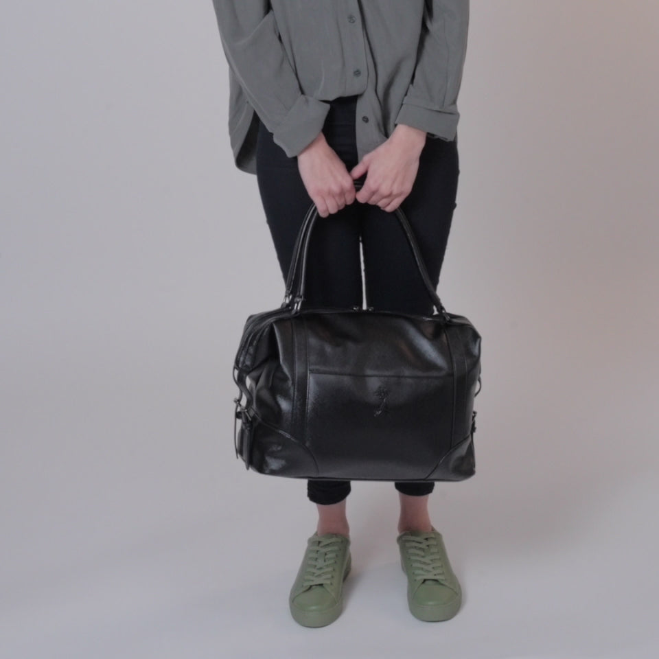 Model wearing black leggings, denim shirt and green leggings using the  trolley sleeve on the Bambino - Black Changing bag and carrying the bag over the shoulder with the two long handle carry straps.