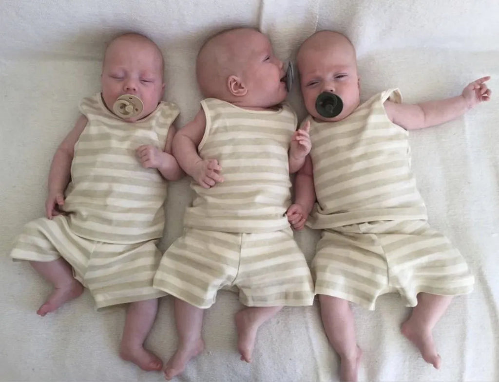 Triplets wearing a matching baby vest and shorts